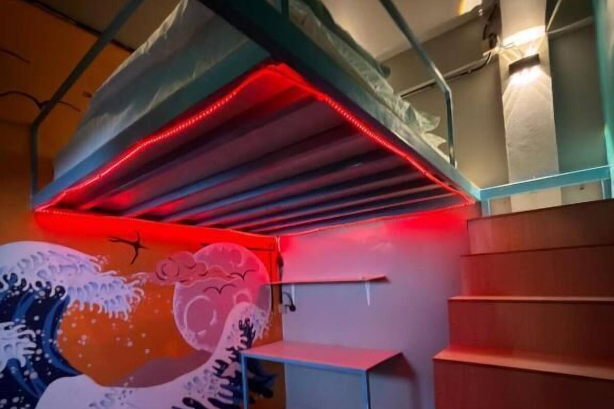 Una scala con illuminazione rossa, una ringhiera in metallo e un muro decorato con un murales a forma di onda.