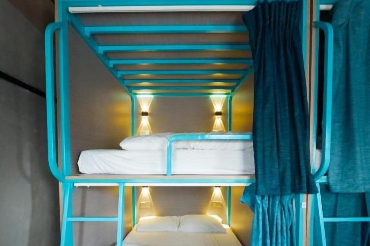 Una cama litera con escalera, cortina y dos luces fijadas a la pared.
