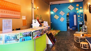 Un espace d’accueil avec un comptoir où sont exposées des photos, un mur bleu orné de motifs décoratifs et un escalier menant à un autre étage.
