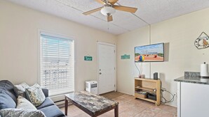 A living room with a sofa, coffee table, ceiling fan, TV, and a door marked "BEACH". - Beach Block steps to sand and many more attractions making this the perfect spot (Wildwood)
