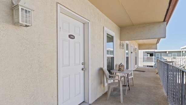 A covered outdoor area with a white door marked "306", a small table with chairs, and a lantern on the wall. - Beach Block steps to sand and many more attractions making this the perfect spot (Wildwood)