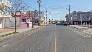 A street with a pink storefront, a green vehicle, and a building with a 'Parking' sign. - Beach Block steps to sand and many more attractions making this the perfect spot (Wildwood)