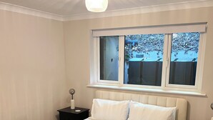 Un dormitorio con una cama grande, una ventana que da a vistas exteriores, un radiador y una mesita de noche con una lámpara.