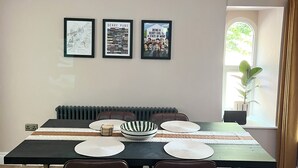 Un comedor con una mesa negra, dos sillas marrones, una araña y tres cuadros en la pared.
