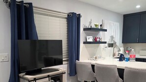 Ett modernt kök med en matplats, en tv placerad på ett träställ och en barstol.