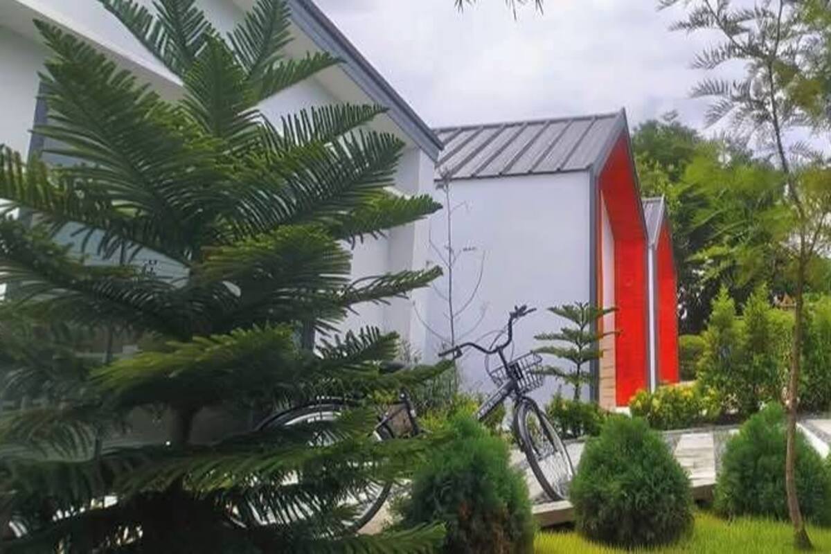 Un bâtiment moderne avec des touches de rouge, entouré d’une végétation luxuriante et bordé d’un sentier.