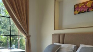 Una cama bien tendida con peluches, una ventana con cortinas y un cuadro en la pared.