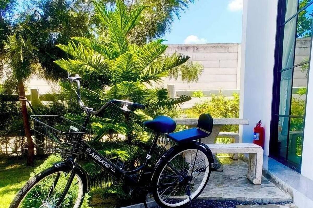 Un vélo est garé sur un chemin de béton parsemé de petits cailloux, à proximité d’un banc et d’un bâtiment doté de grandes fenêtres.