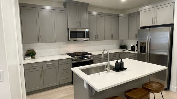 A modern kitchen with grey cabinets, a stainless steel refrigerator, a microwave, and a sink with bar stools. - Charming 3-bedroom townhome with WiFi, AC in wonderful Washington (Washington)