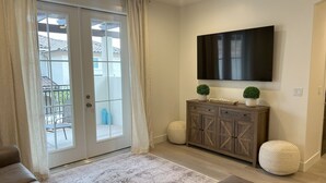 A living room with a sliding glass door, a flat-screen TV mounted on the wall, a wooden cabinet, two round poufs, and a patterned rug. - Charming 3-bedroom townhome with WiFi, AC in wonderful Washington (Washington)