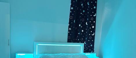 A bedroom with a bed, a nightstand, and a wall-mounted light.