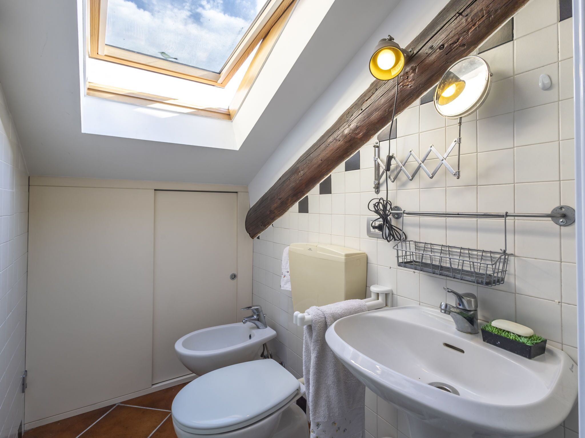 A bathroom with a skylight, a bidet, a toilet, a sink, and a towel rack.