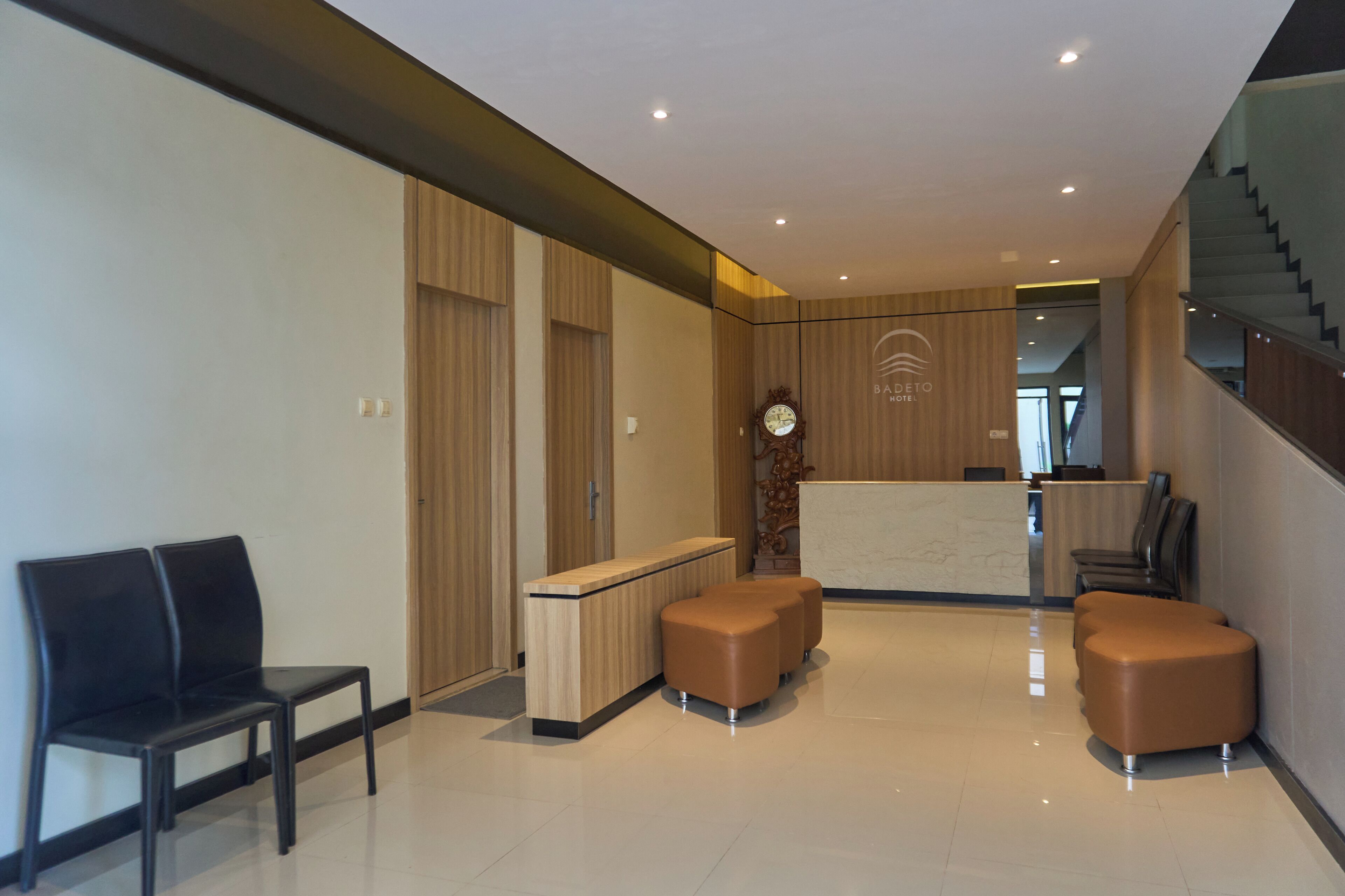 A modern hotel lobby with a reception desk, seating area, and a staircase.