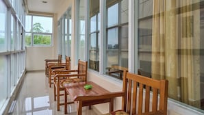 Un pasillo con una fila de sillas y mesas de madera, ventanas grandes y vistas a zonas verdes al exterior.