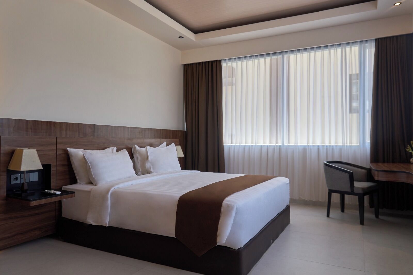 A modern hotel room with a large bed, a desk, and a chair.