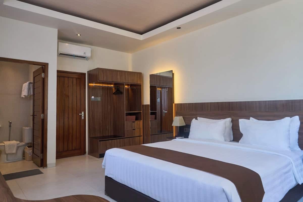 A hotel room with a large bed, wooden wardrobe, and a mirror.