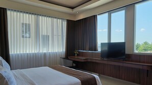 Una habitación de hotel con cama, televisor sobre un mueble de madera y un ventanal con cortinas.