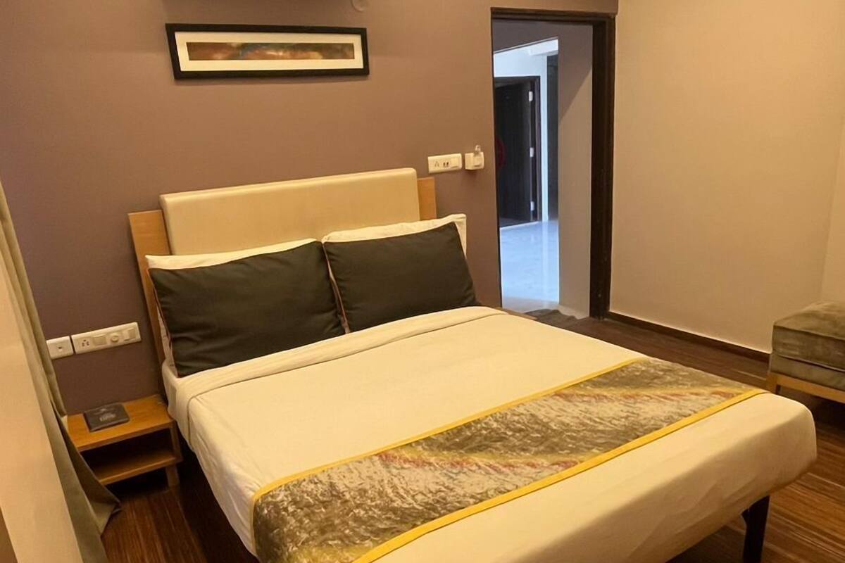 Quarto de hotel moderno com uma cama grande, ventilador de teto, aparelho de ar condicionado, quadro emoldurado na parede e piso de madeira.