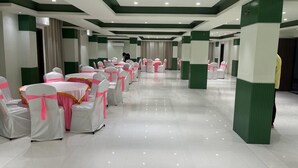 Un amplio salón con filas de mesas y sillas, una decoración en tonos verde y blanco, y un suelo pulido.
