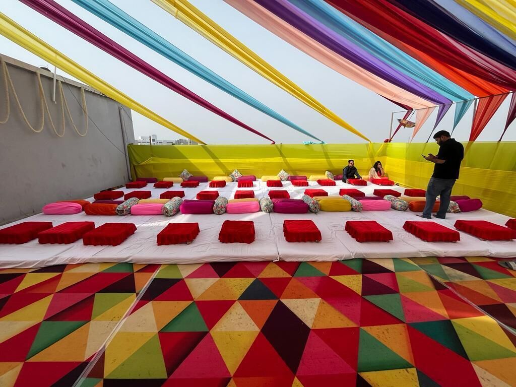 A rooftop event space with a colorful geometric-patterned floor, a white tablecloth, and a variety of cushions and pillows.