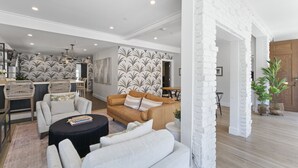 A spacious living room with a modern design, featuring a sofa set, a coffee table, and a dining area with a wooden table and chairs.