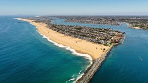 An aerial view of a coastal town with a long sandy beach, a rocky breakwater, and a dense cluster of buildings along the shore.