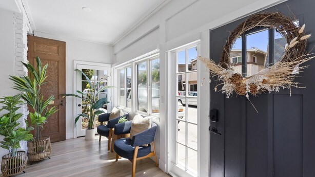 A bright hallway with a dark door, a woven wreath, and two chairs with cushions.