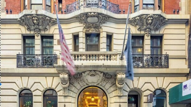 A historic building with ornate architectural details, a prominent entrance, and flags.