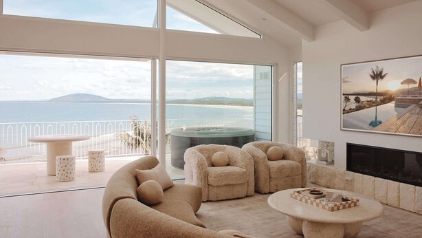 A modern living room with a large window overlooking a beach and ocean, a cozy sofa, two armchairs, a round coffee table, and a fireplace. - Isola Gerroa (Gerroa)