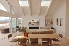 A modern living room with a large round table, comfortable seating, a fireplace, and a view of the outdoors.