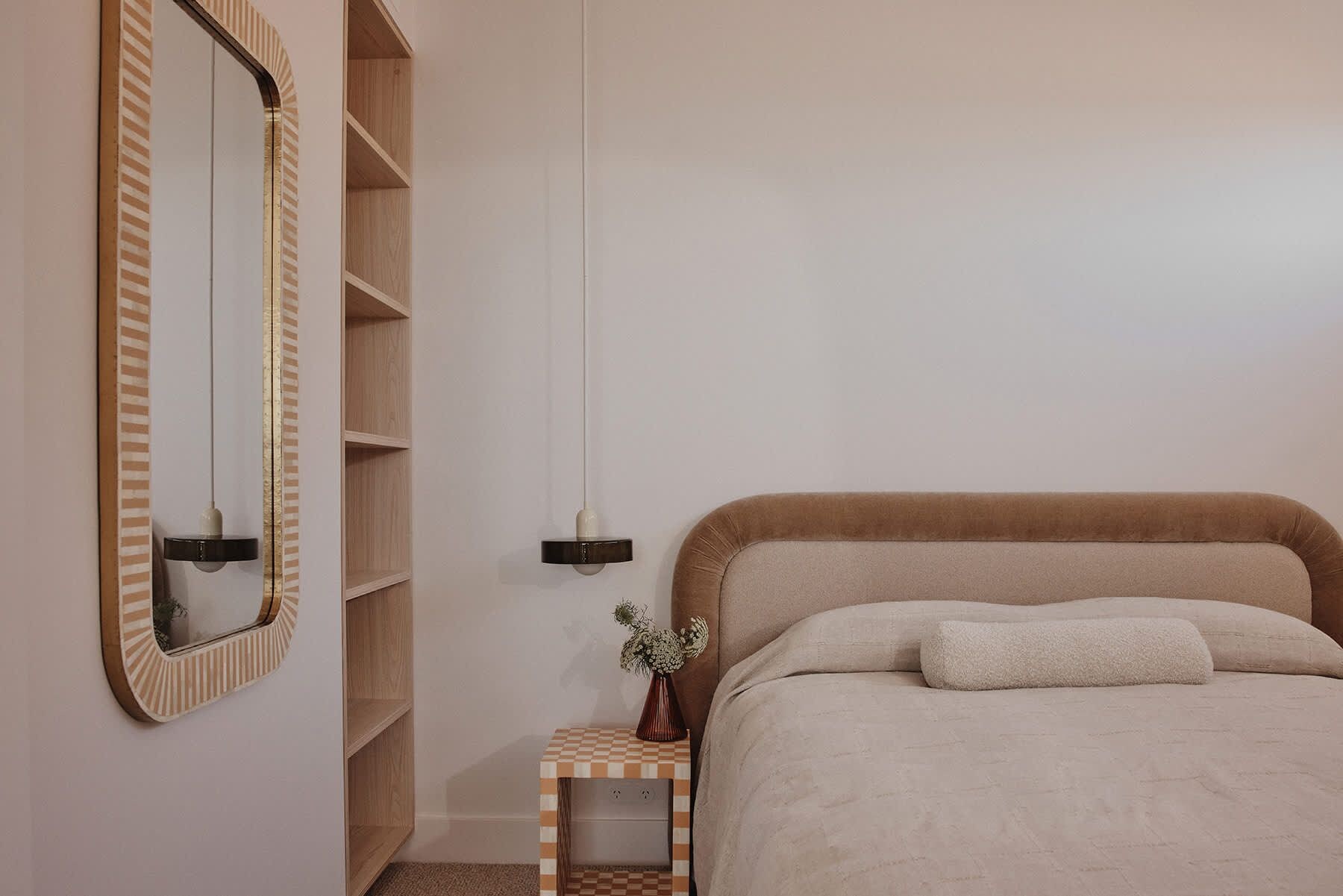 A bedroom with a bed, a bedside table, a mirror, and a hanging light fixture.