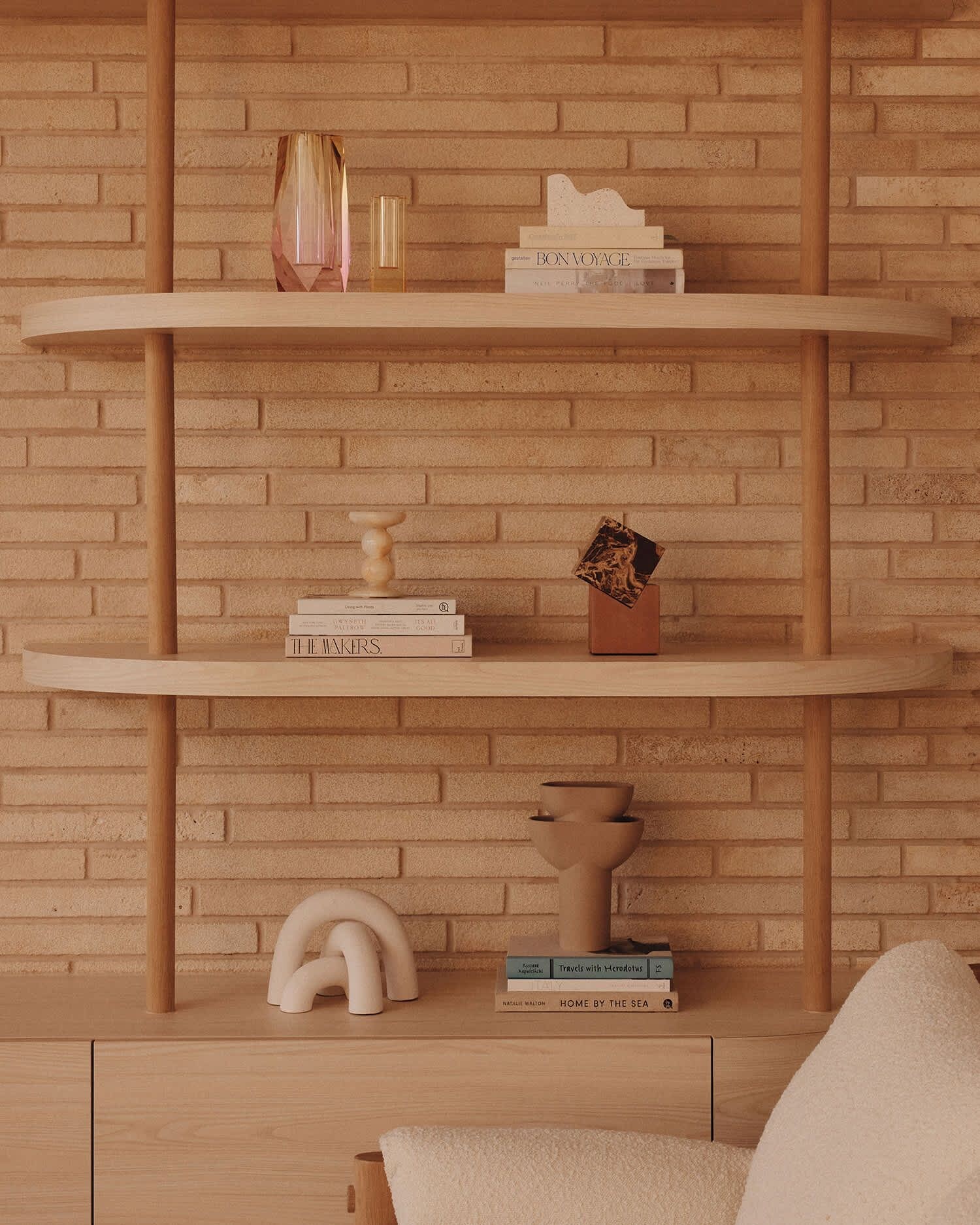 A wooden bookshelf against a brick wall with books and decorative items.