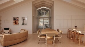 Uma sala de estar ampla com um sofá grande, uma mesa de jantar com cadeiras e uma cozinha com banquetas.