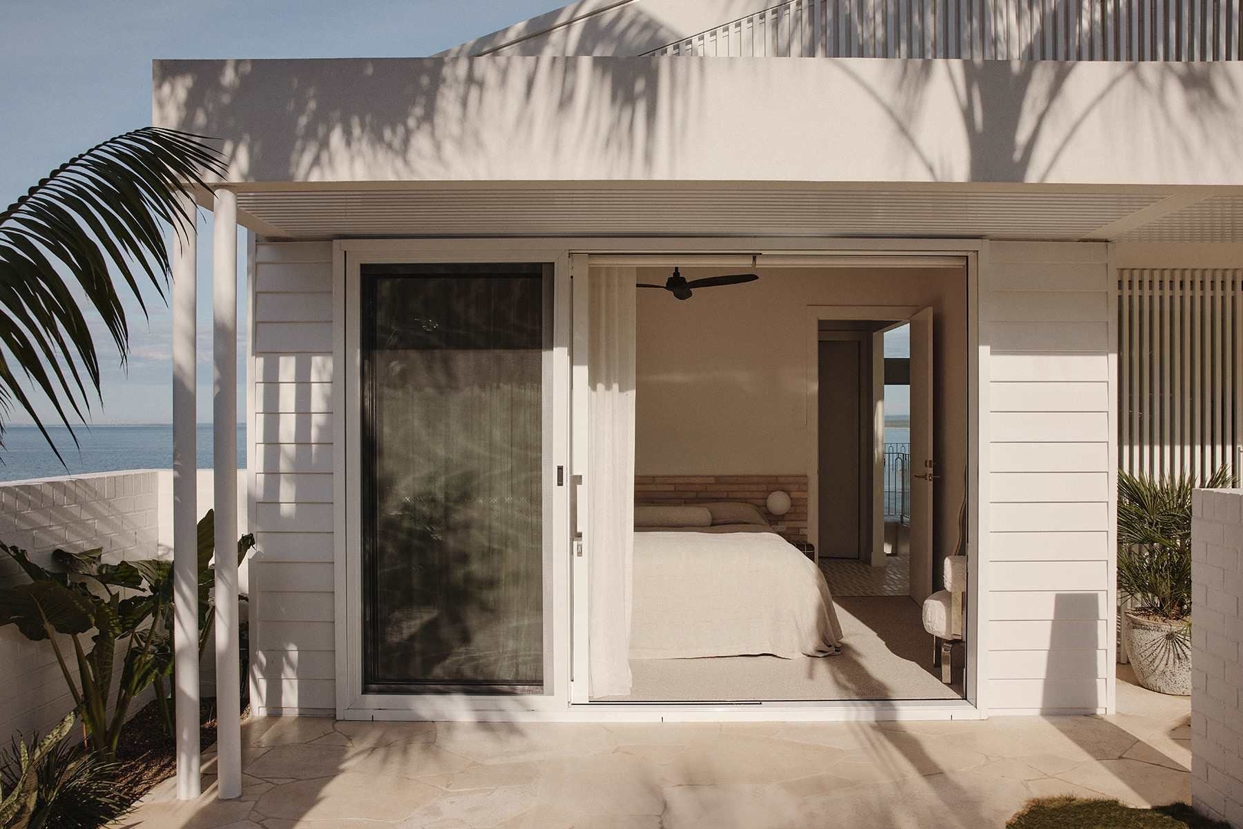 A modern house with a sliding glass door leading to a bedroom with a bed and a nightstand.