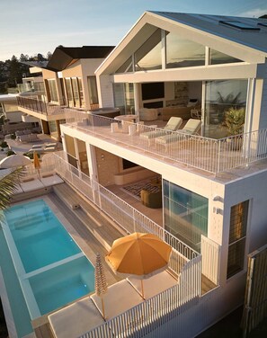 Uma casa moderna de vários andares com piscina no terraço, área de estar ao ar livre e varanda com guarda-corpo de vidro.