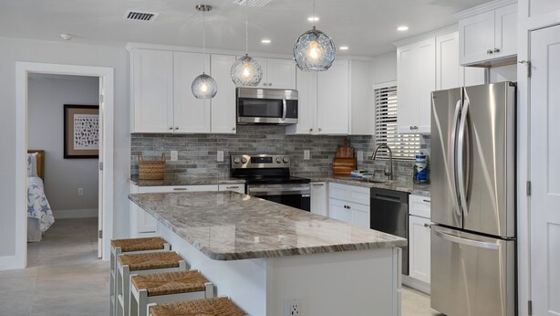 A modern kitchen with white cabinets, a stainless steel refrigerator, a microwave, and a large island with bar stools. - Blind Pass C106  | Upgraded Ground Floor Residence at Blind Pass | Steps to Pool (Sanibel)