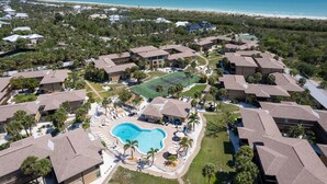 An aerial view of a resort with a swimming pool, tennis courts, and beachfront access. - Blind Pass C106  | Upgraded Ground Floor Residence at Blind Pass | Steps to Pool (Sanibel)