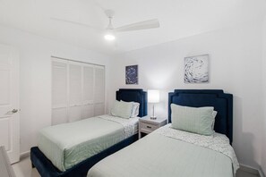 Un dormitorio con dos camas, un ventilador de techo, una mesita de noche con lámpara y un armario.