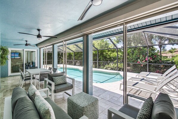 A sunlit patio with a pool, outdoor furniture, and a ceiling fan.