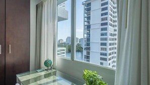 Una habitación moderna con un ventanal grande, una mesa de vidrio y vista a un edificio alto.