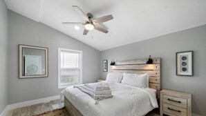 Un dormitorio con cama, mesita de noche, ventilador de techo y cuadros en las paredes.