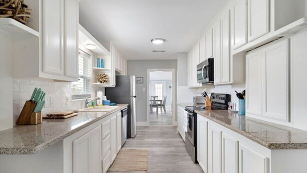 Una cocina moderna con armarios blancos, encimeras de granito y electrodomésticos de acero inoxidable.