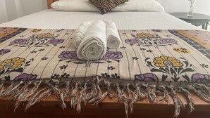 A neatly made bed with a floral-patterned bedspread and a rolled white towel. - Eagles Eco Lodge - Kandy (Teldeniya)