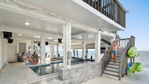 A covered outdoor swimming pool with steps leading down to the water, a staircase to the beach, and a view of the ocean.