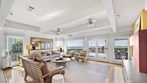 A spacious living room with a large window overlooking the ocean, furnished with a sofa, chairs, and a coffee table.