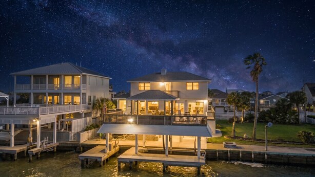 A waterfront property with multiple levels, a dock, and a view of the night sky.