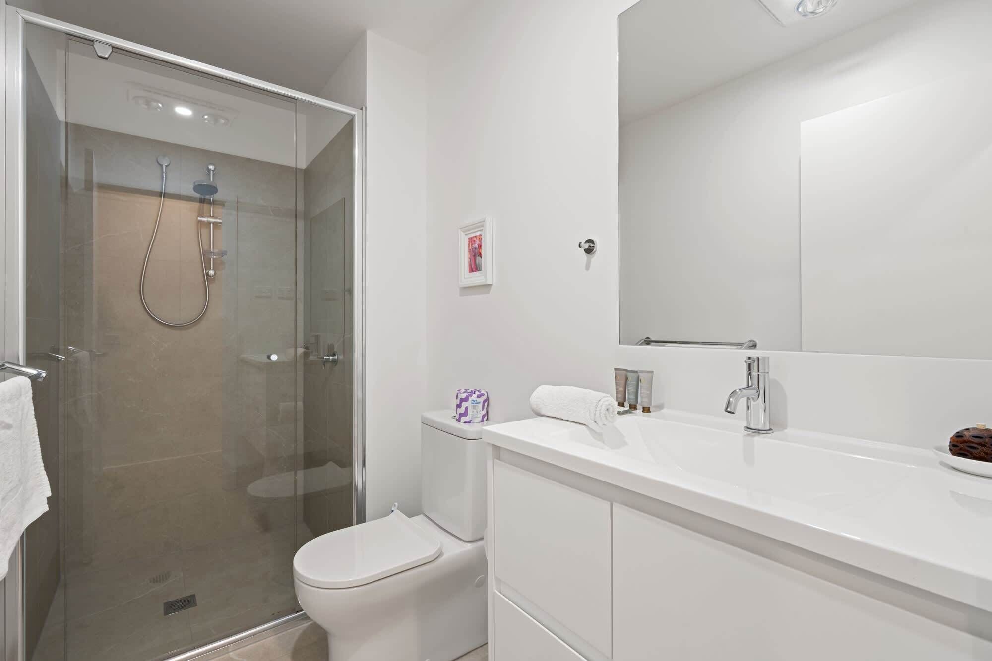 Une salle de bain moderne avec une douche à parois de verre, des toilettes blanches et un meuble-lavabo avec un miroir.