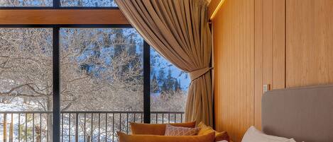 A bedroom with a large window, a bed, and a seating area with cushions.