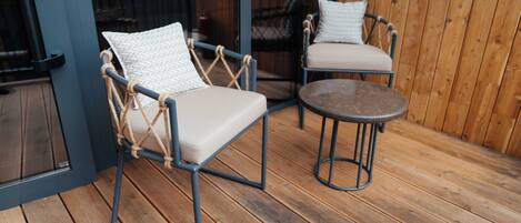 Una terraza de madera con dos sillas y una mesa redonda pequeña.