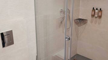 Een moderne badkamer met een douchecabine van glas, een toilet en een plank met toiletartikelen.